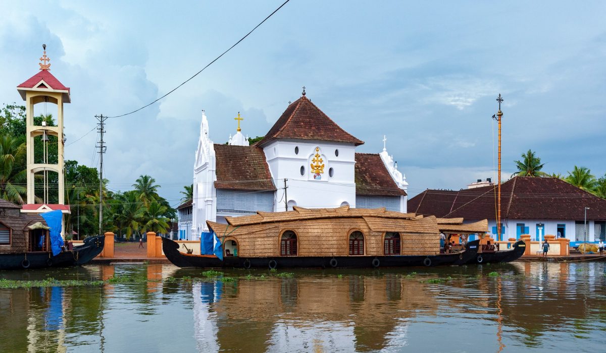 Tourist rice barge (houseboat) moored near a Christian Church on the inland waterways of the Kerala Backwaters, near Kochi in southern India.